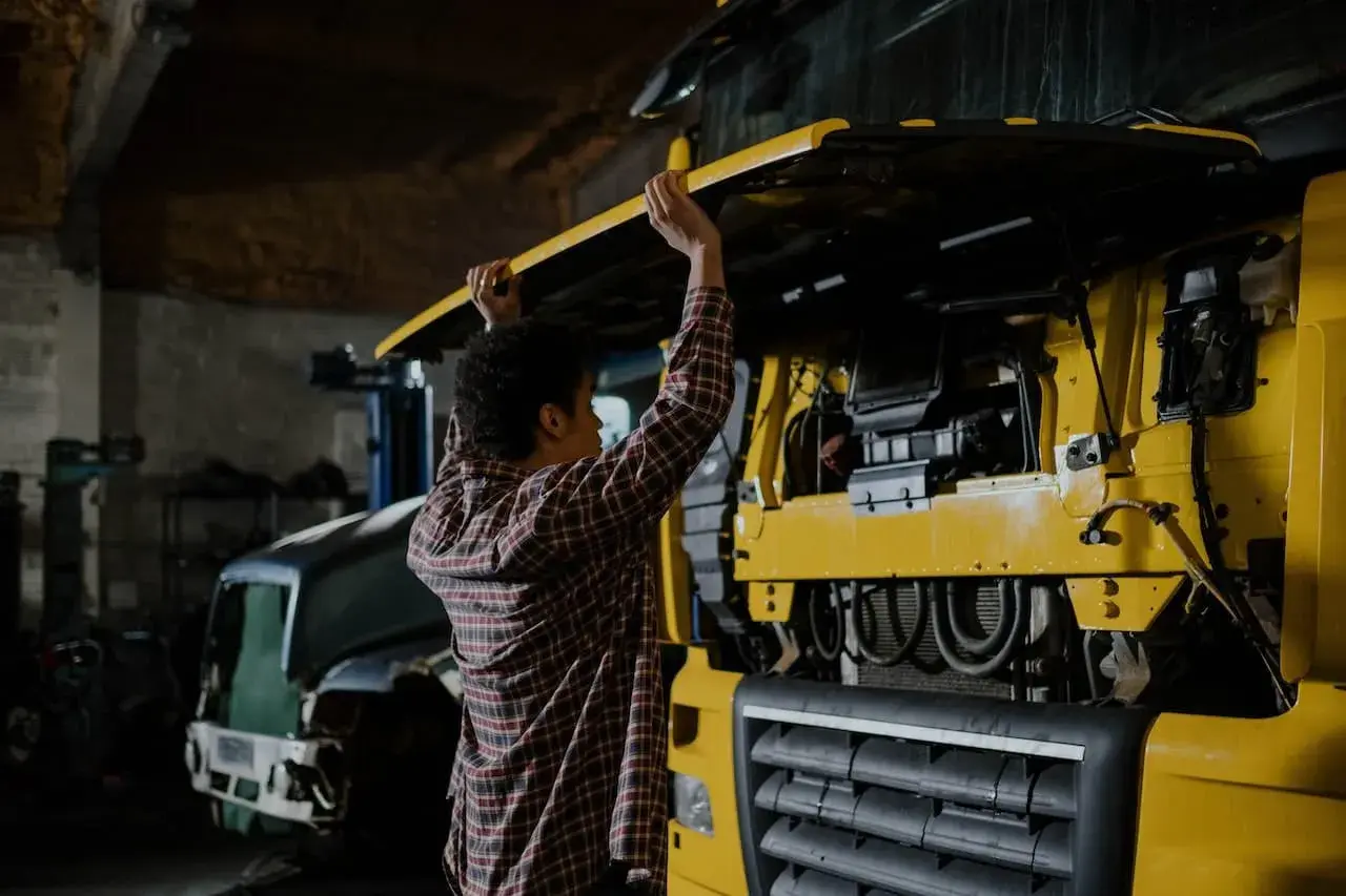 Un mécanicien examine les différentes parties d'un camion jaune, soulevant le capot pour accéder au moteur.