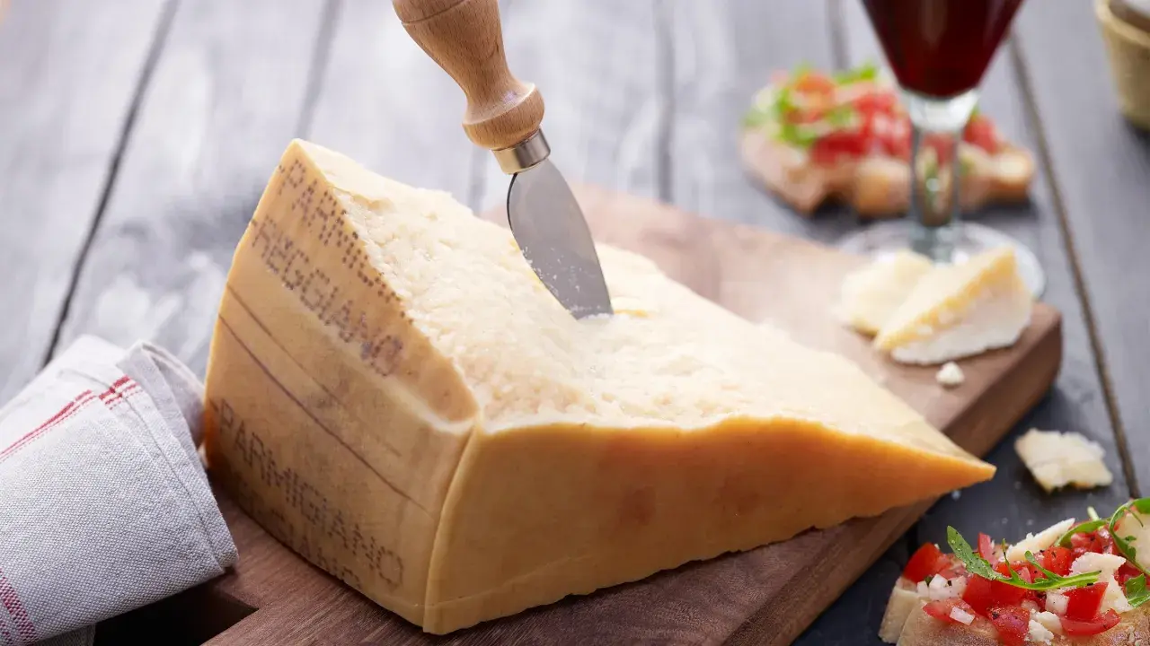 Ein großes Stück Parmesan mit einem Messer, daneben Bruschetta und ein Glas Rotwein.