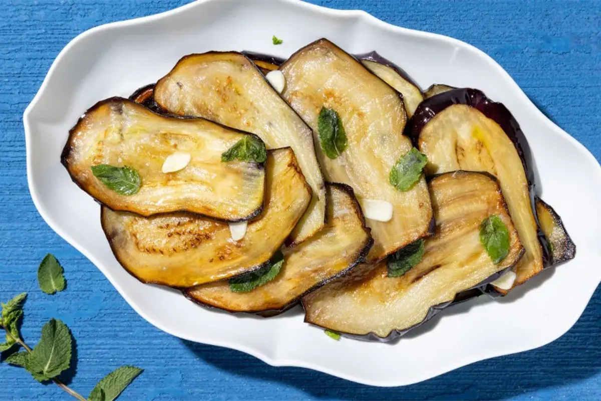 Fette di melanzane grigliate, guarnite con menta fresca e aglio. Un contorno di verdure semplice e gustoso.