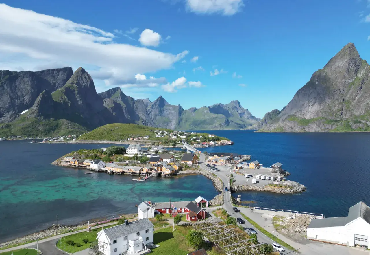 Idyllisches Dorf an der Küste mit roten und weißen Häusern, umgeben von majestätischen Bergen. Tolle Lofoten Tipps für Ihren Urlaub!