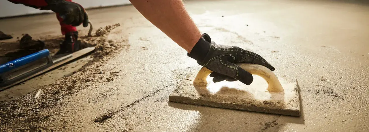 Arbeiter verlegt Estrich mit Glättkelle. Der frische Estrich wird sorgfältig bearbeitet, um eine ebene Fläche zu schaffen.