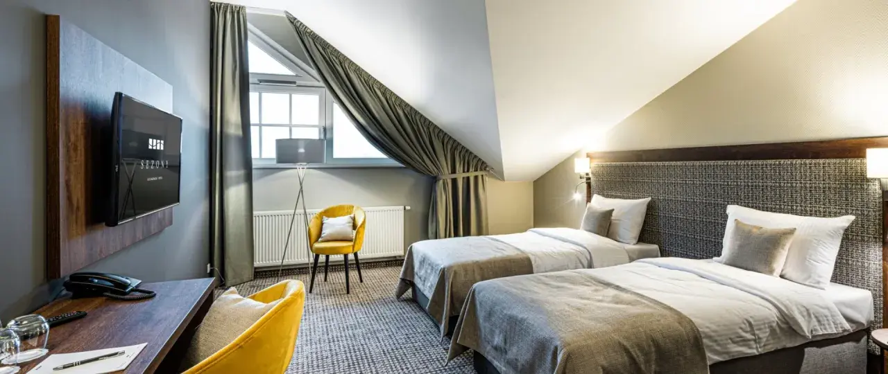 Pokój hotelowy z dwoma łóżkami, żółtym fotelem i biurkiem. Idealne miejsce na nocleg, gdzie gwiazdki w hotelach są gwarancją komfortu.