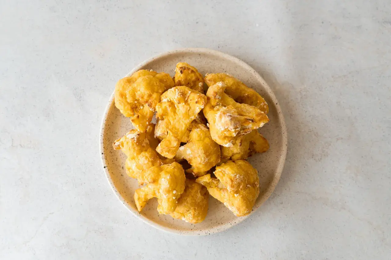 Alitas de coliflor doradas y crujientes en un plato, listas para disfrutar.