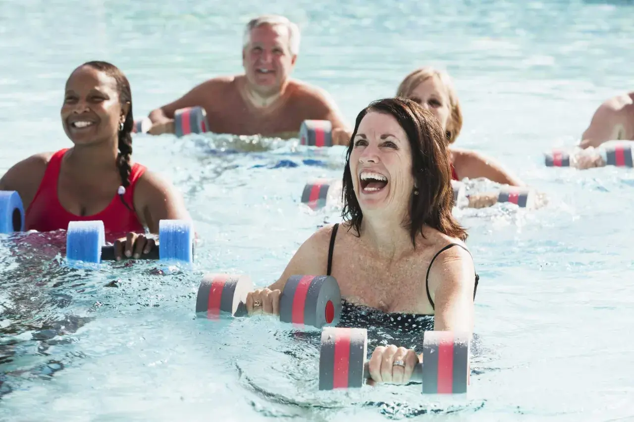 Personas sonriendo y haciendo aqua gym en una piscina con pesas flotantes.
