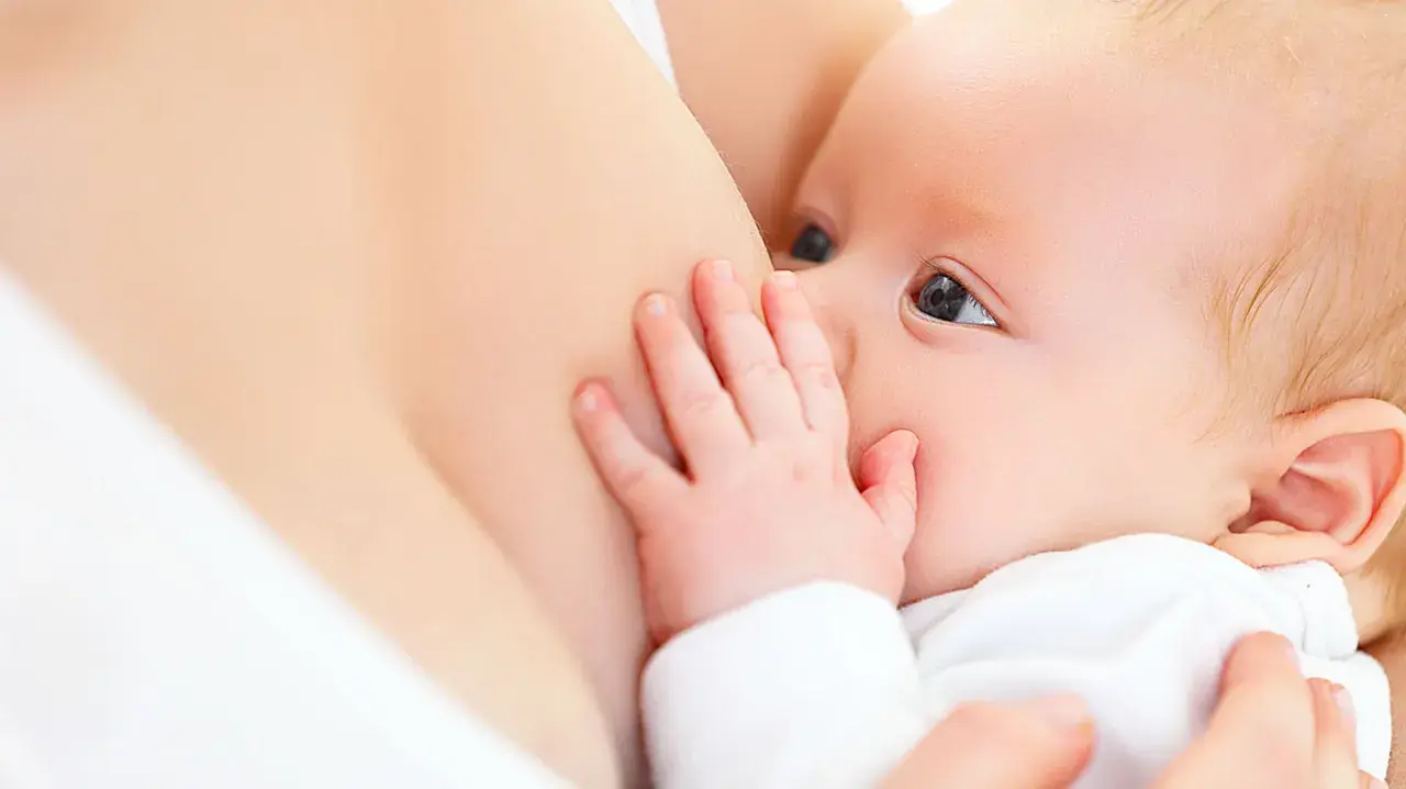 Ein Baby trinkt an der Brust. Die Hand des Babys ruht auf der Brust, was die Milchproduktion anregen kann.