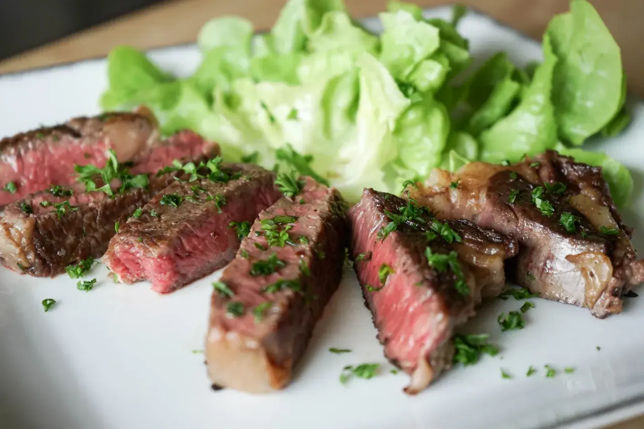 Tranches de steak black angus saignant, garnies de persil frais, servies avec de la laitue croquante sur une assiette blanche.