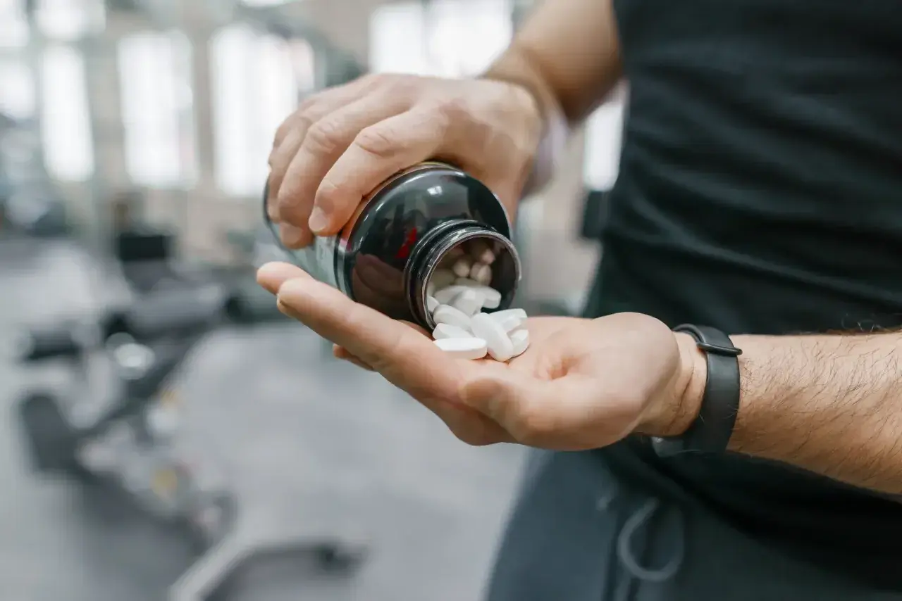 Mann schüttet weiße Pillen aus einer Flasche in seine Hand. Möglicherweise zur Unterstützung der Yohimbin Wirkung im Fitnessstudio.