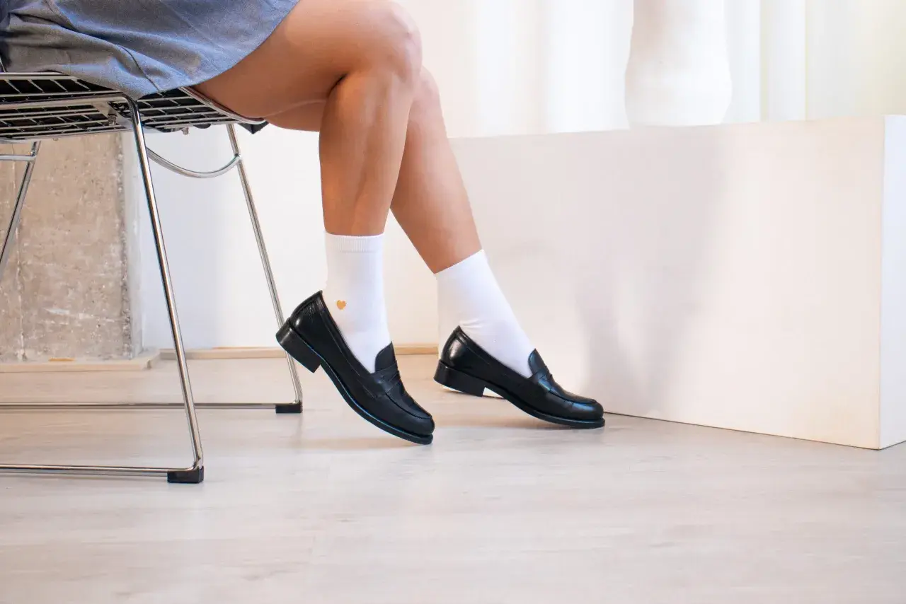 Une tenue chic avec mocassin femme noir, chaussettes blanches et une jupe grise. Parfait pour un look décontracté et élégant.
