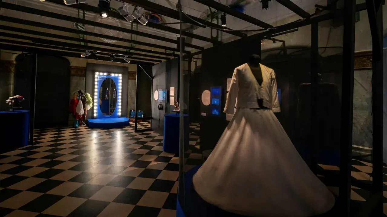En vit dansklänning visas upp i en monter på Dansmuseet Stockholm. Golvet har ett schackrutigt mönster.