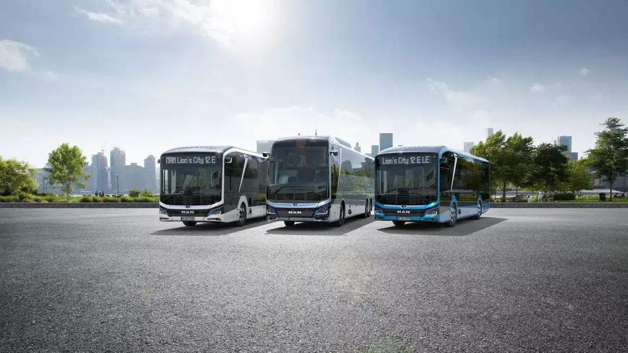 Trzy nowoczesne autobusy elektryczne MAN Lion's City E stoją na tle miejskiej panoramy.