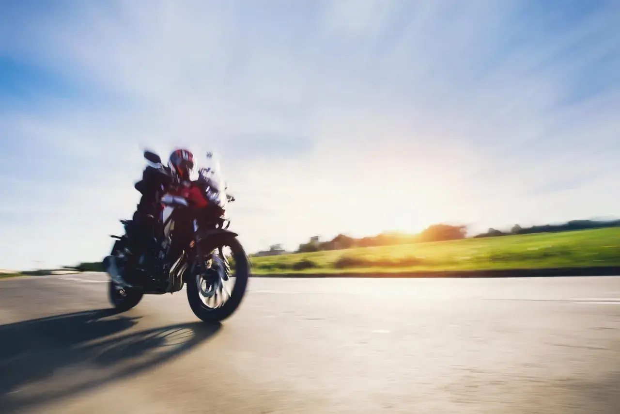 Motocyklista w kasku pędzi drogą, ciesząc się pięknym zachodem słońca. To idealny **sezon motocyklowy**!
