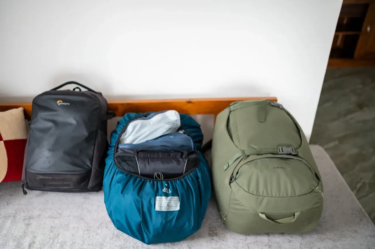 Drei Rucksäcke bereit für das Abenteuer. Ein schwarzer Lowepro, ein blauer mit Regenhülle und ein grüner Porter 65 – perfekt für das Asien Backpacking.