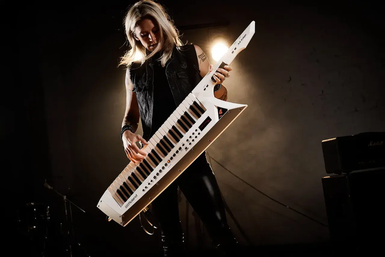 Kobieta gra na białym keyboardzie na pasku, który wygląda jak gitara.