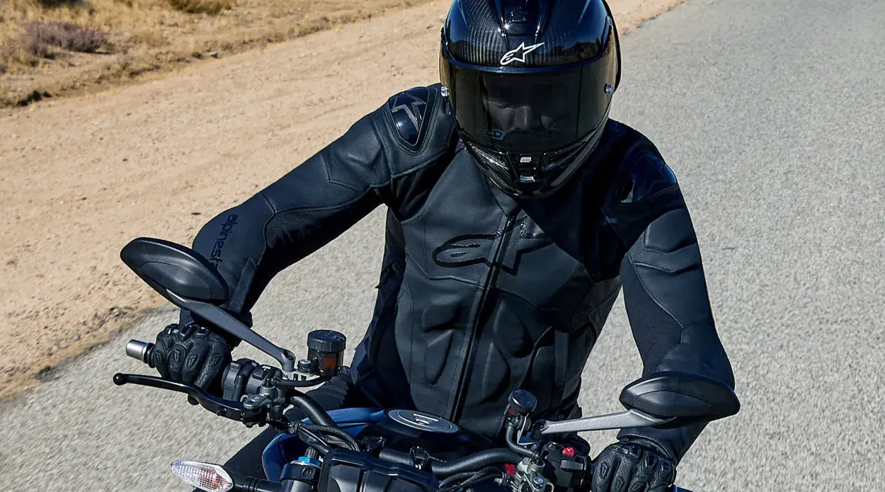 Motocyklista w kasku i czarnej kurtce Alpinestars jedzie po pustynnej drodze.
