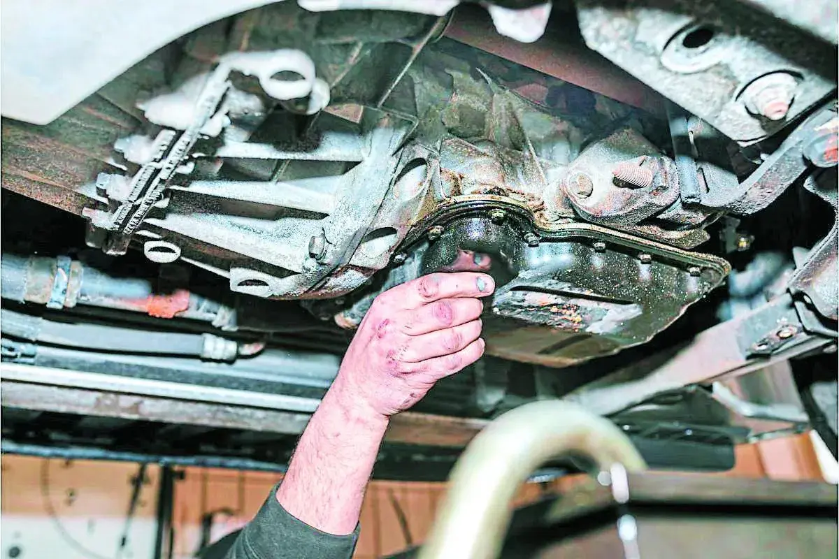 Mano revisa el cárter de un coche, mostrando signos de perdida de aceite.