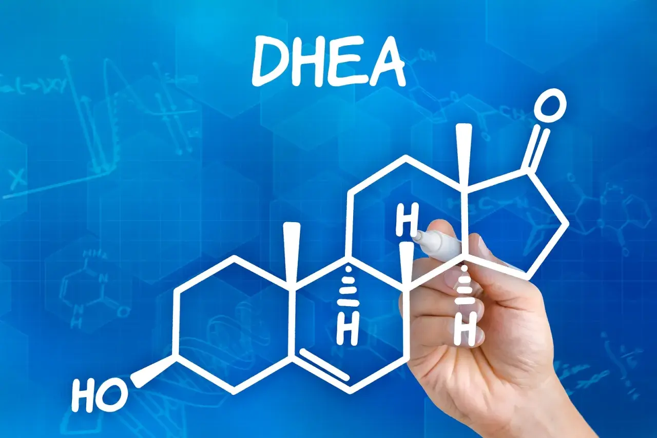 DHEA co to? Rysunek przedstawia wzór chemiczny DHEA, hormonu steroidowego, z ręką piszącą markerem.
