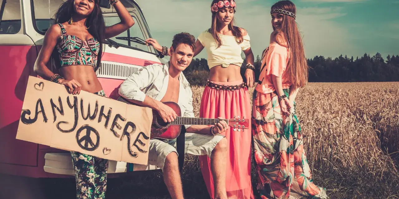Neo-Hippies mit Gitarre und Schild "Anywhere" vor einem Van in einem Feld.