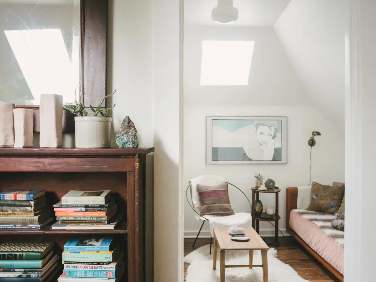 Accogliente libreria in mansarda con un letto, una poltrona e un quadro.