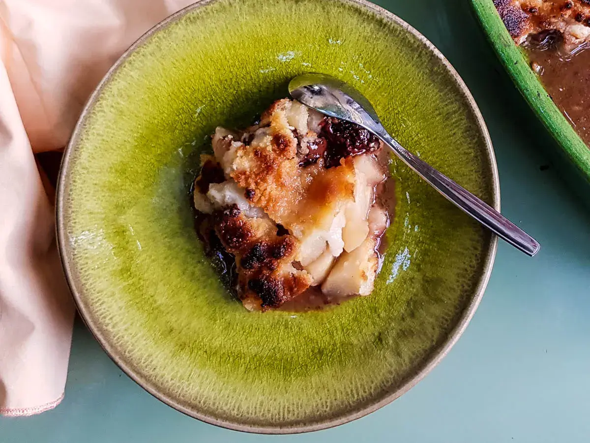 Un délicieux crumble poire chocolat, doré et croustillant, servi dans une assiette verte avec une cuillère.