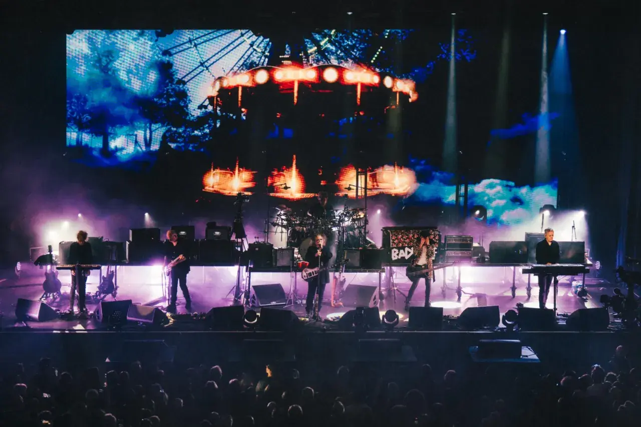 The Cure Polska na żywo. Zespół gra na scenie, w tle wielki ekran z karuzelą.