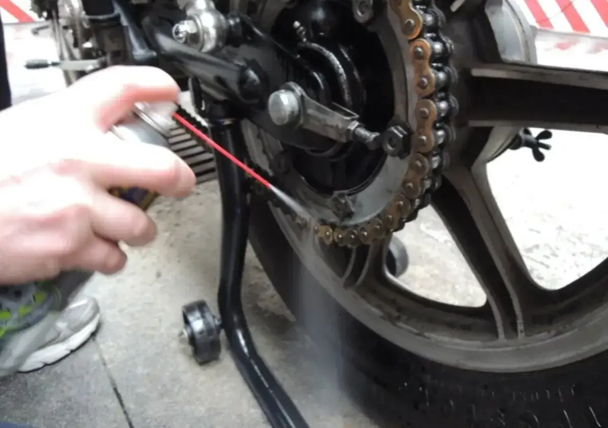 Mano spruzza spray sulla catena della moto per pulirla.