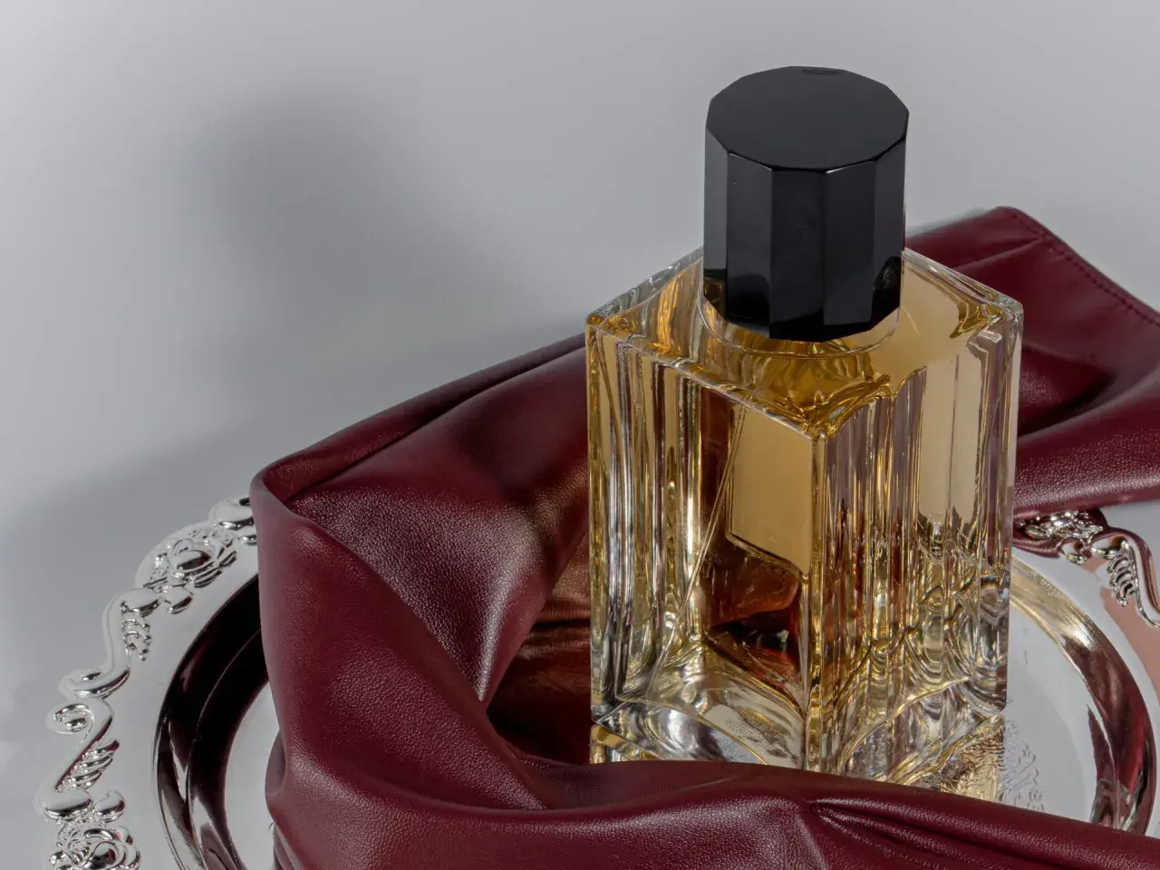 Elegancka butelka perfum na ozdobnej tacy, otulona bordową skórą. To wyjaśnia, dlaczego znana modelka nigdy nie używa tradycyjnych perfum z drogerii.