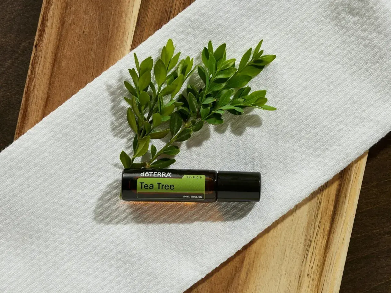 Aceite árbol de té roll-on, con hojas verdes. Considera las contraindicaciones antes de usar.
