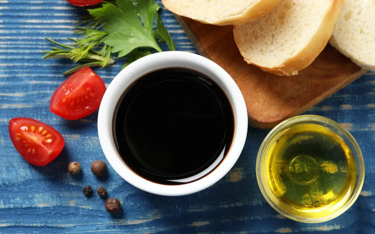 Sos do czego? Ocet balsamiczny, oliwa, pomidorki i pieprz na niebieskim tle. Idealne składniki na pyszną sałatkę.