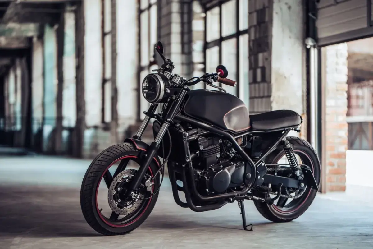 Elegante moto customizada, negra y con detalles rojos, lista para la aventura. Una moto sin papeles que inspira libertad y rebeldía.