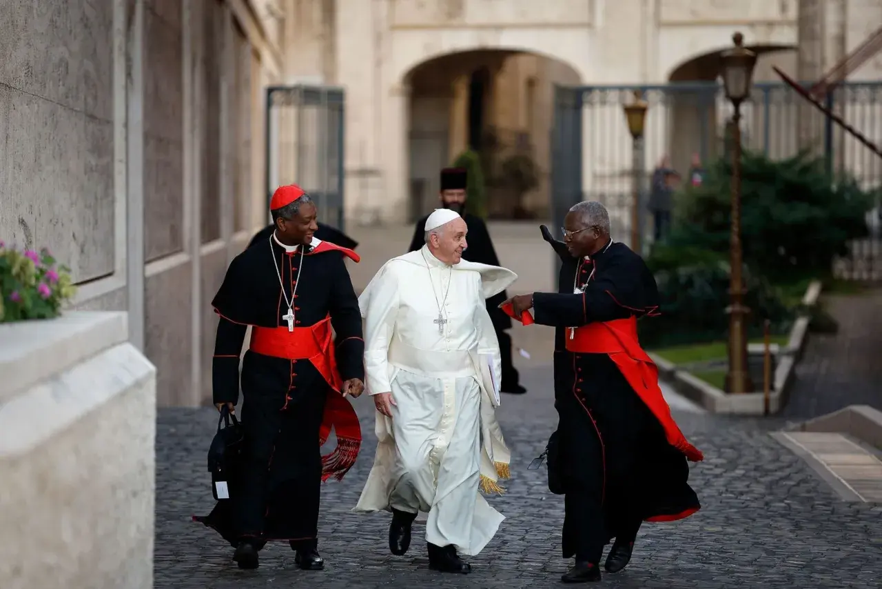 Papst Franziskus geht mit zwei Kardinälen. Was macht der Papst den ganzen Tag? Er spricht, betet und kümmert sich um die Menschen.