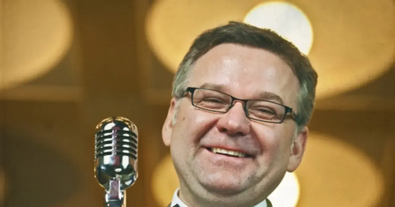 Artur nagrał płytę myśliwiecka. Uśmiechnięty mężczyzna w okularach stoi przy mikrofonie.