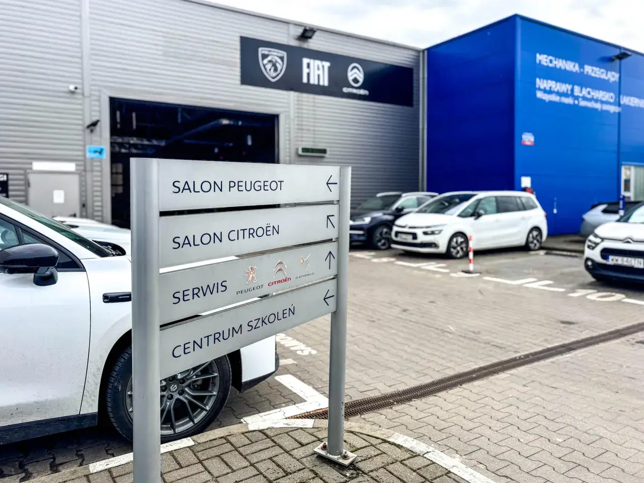 Znak z napisem "Salon Peugeot", "Salon Citroën", "Serwis" i "Centrum Szkoleń" przy salonie samochodowym. ASO skrót.
