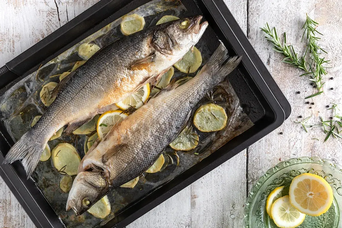 Due branzini al forno su teglia con patate, limone e rosmarino. Un piatto semplice e gustoso pronto per essere servito.
