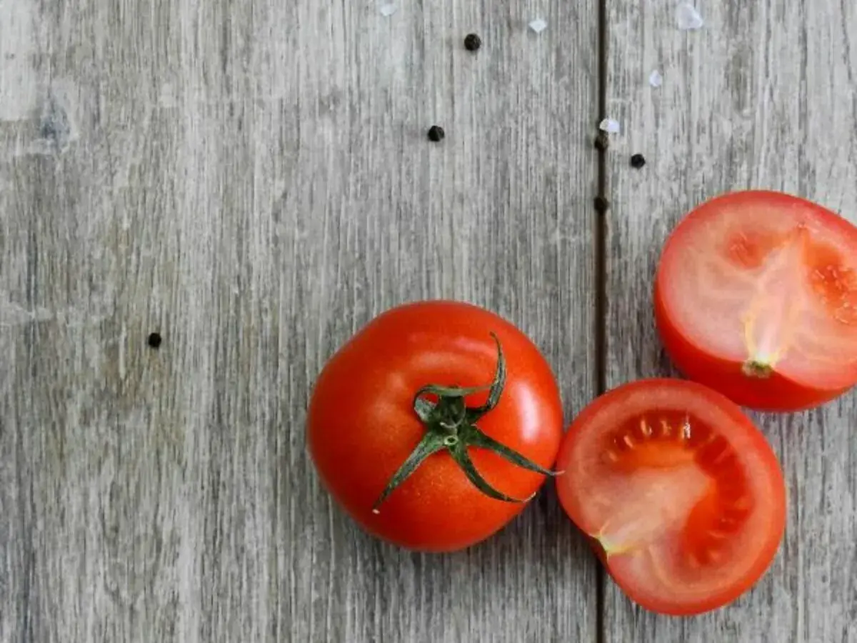 Tomates frescos, uno entero y dos cortados por la mitad, sobre una tabla de madera. Son un ejemplo de 10 alimentos umami.