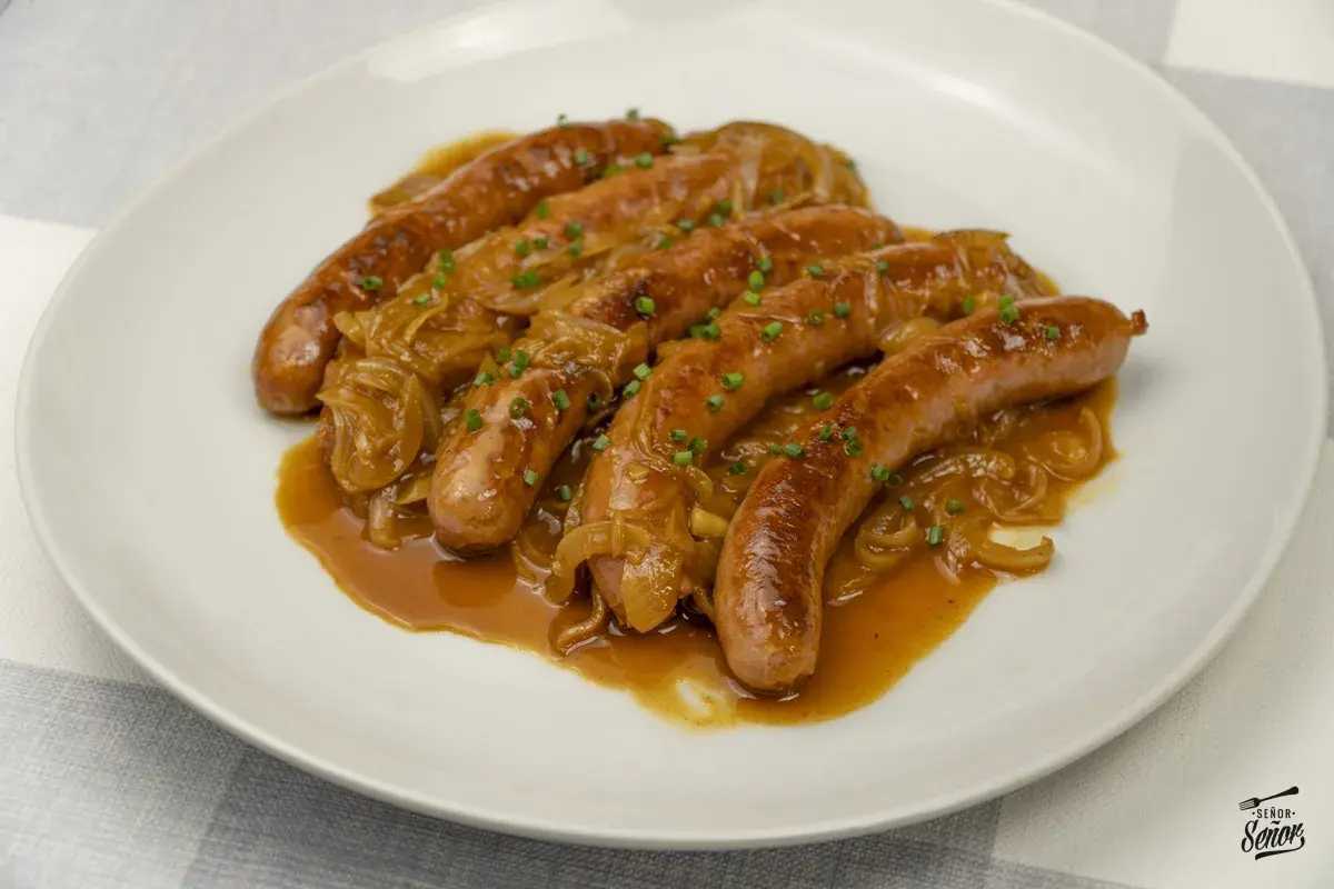 Salchichas doradas en salsa de cebolla caramelizada, un plato delicioso para aprender como hacer salchichas caseras.