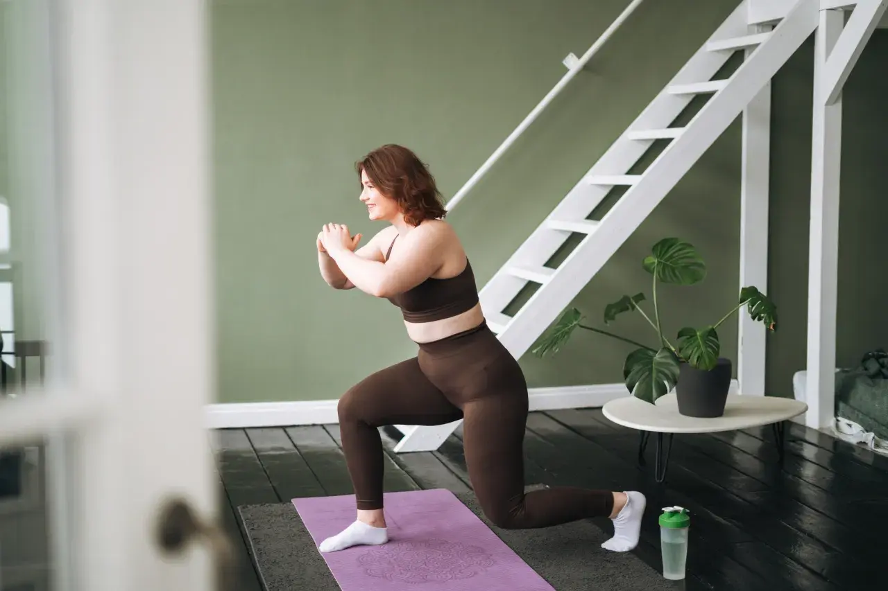 Frau macht einen Ausfallschritt auf einer Matte, ein effektiver bauch workout. Sie trägt braune Sportkleidung und weiße Socken.