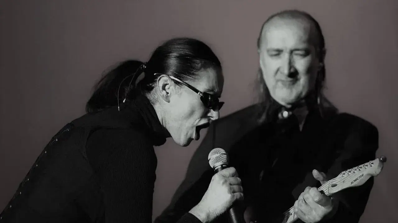 Kora śpiewa do mikrofonu, a obok niej gra na gitarze muzyk. To scena z koncertu, gdzie można usłyszeć maanam piosenki alfabetycznie.