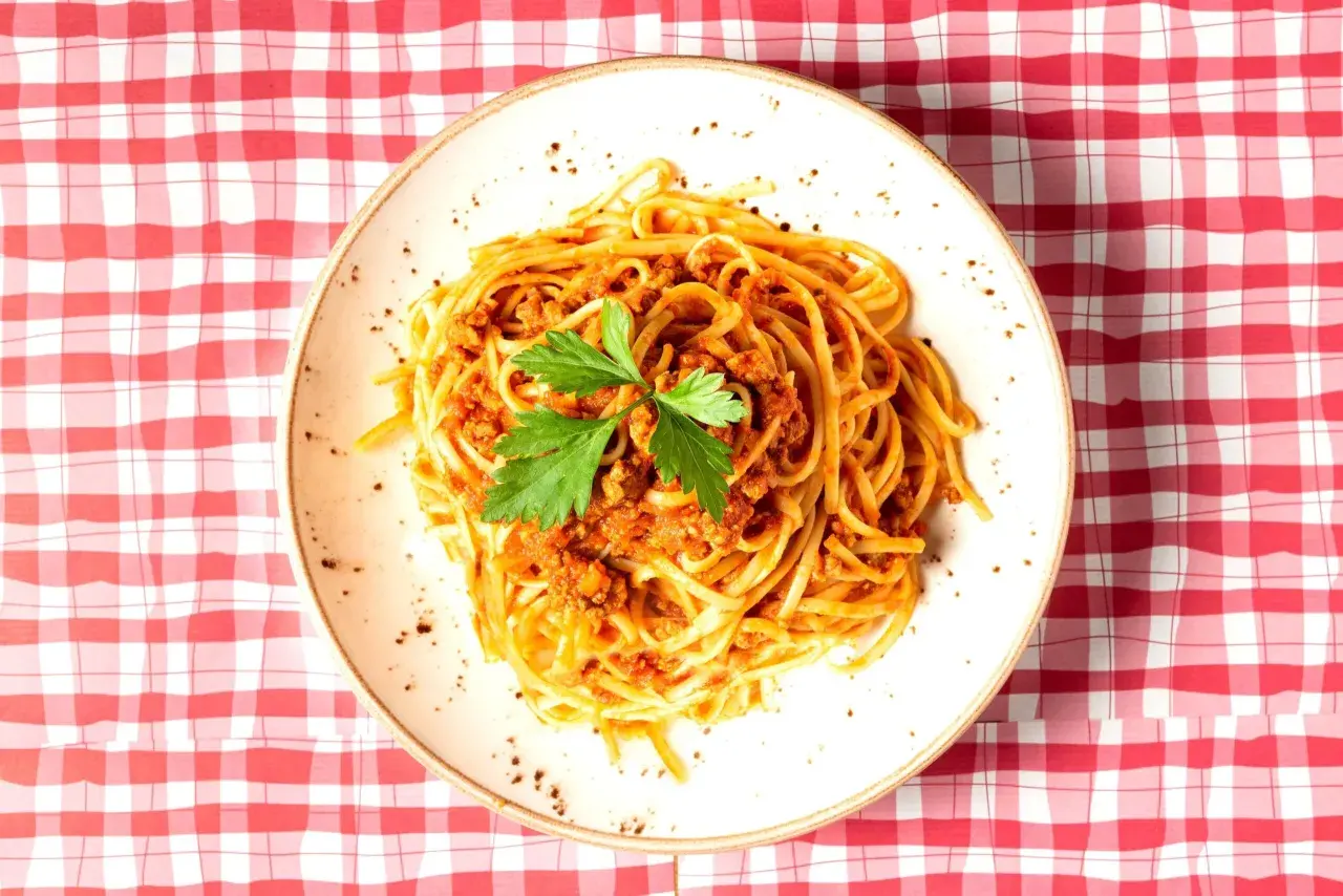 Assiette de spaghetti à la bolognaise, garnie de persil frais, sur une nappe à carreaux rouges et blancs. Une question se pose : peut-on manger des pâtes le soir ?