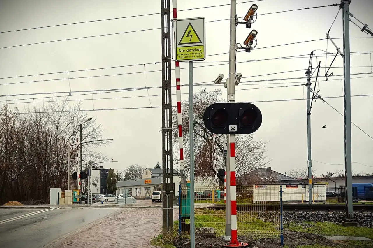 Kamery na przejazdach kolejowych monitorują bezpieczeństwo. Na zdjęciu widać sygnalizację świetlną, rogatki i kamery nadzorujące.