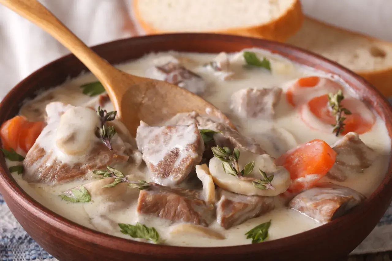 Un réconfortant blanquette de veau facile, servi dans un bol en bois avec une cuillère, garni de persil et de thym.