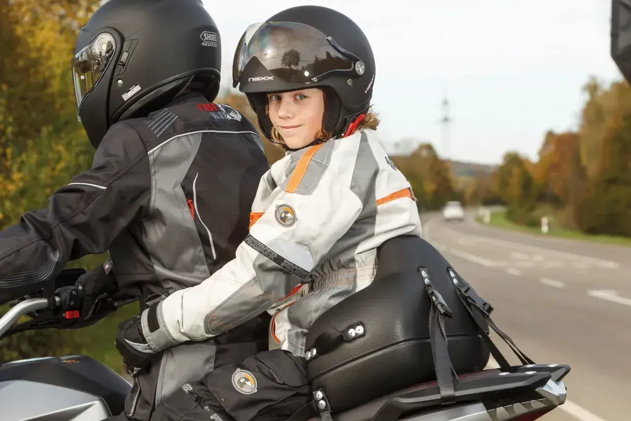 Dziecko w kasku z uśmiechem siedzi z przodu motocykla, gotowe na wspólną podróż. Przewożenie dziecka na motocyklu to przygoda!
