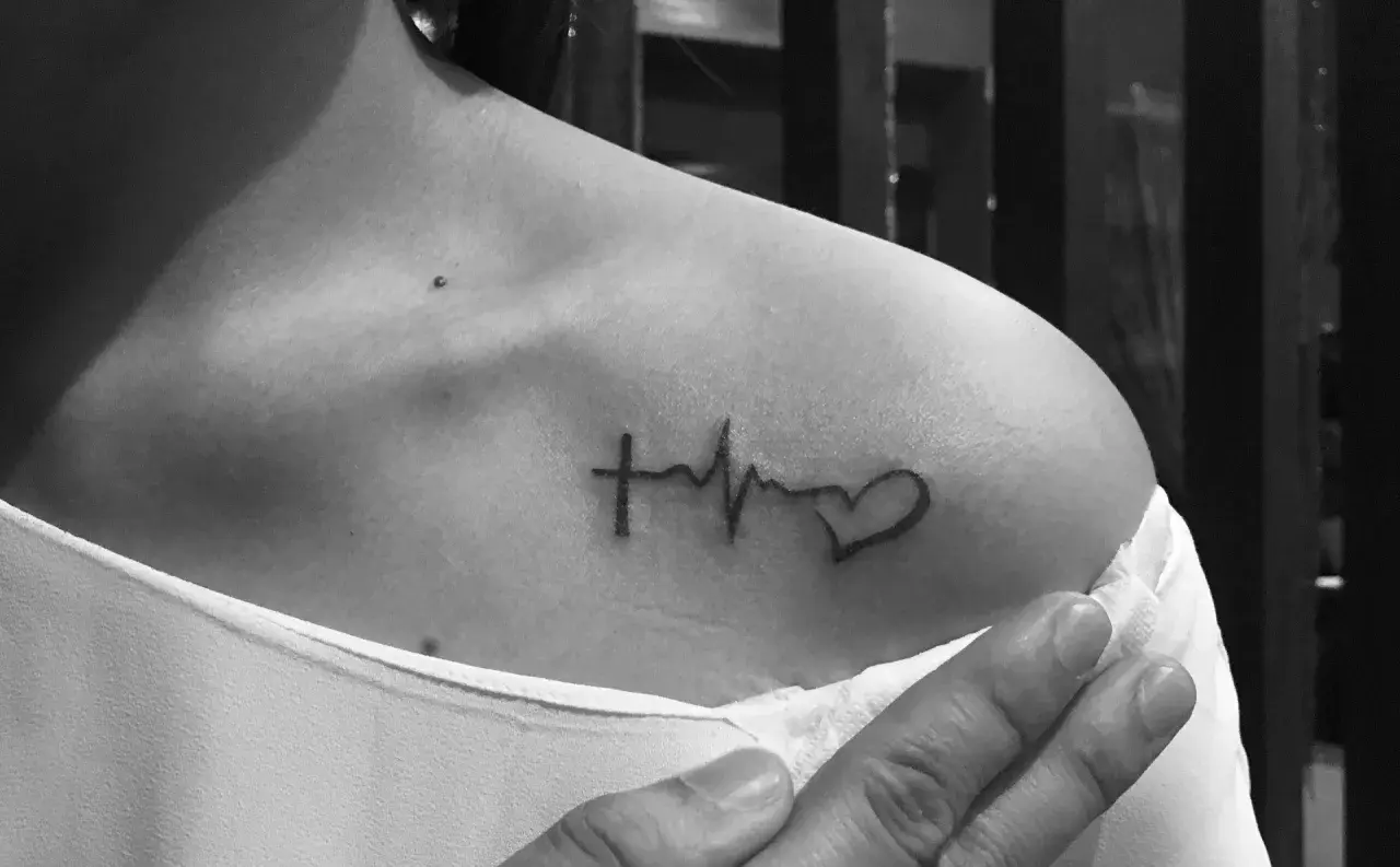 Tatuaż linia życia na ramieniu: krzyż, EKG i serce. Symbol wiary, życia i miłości.