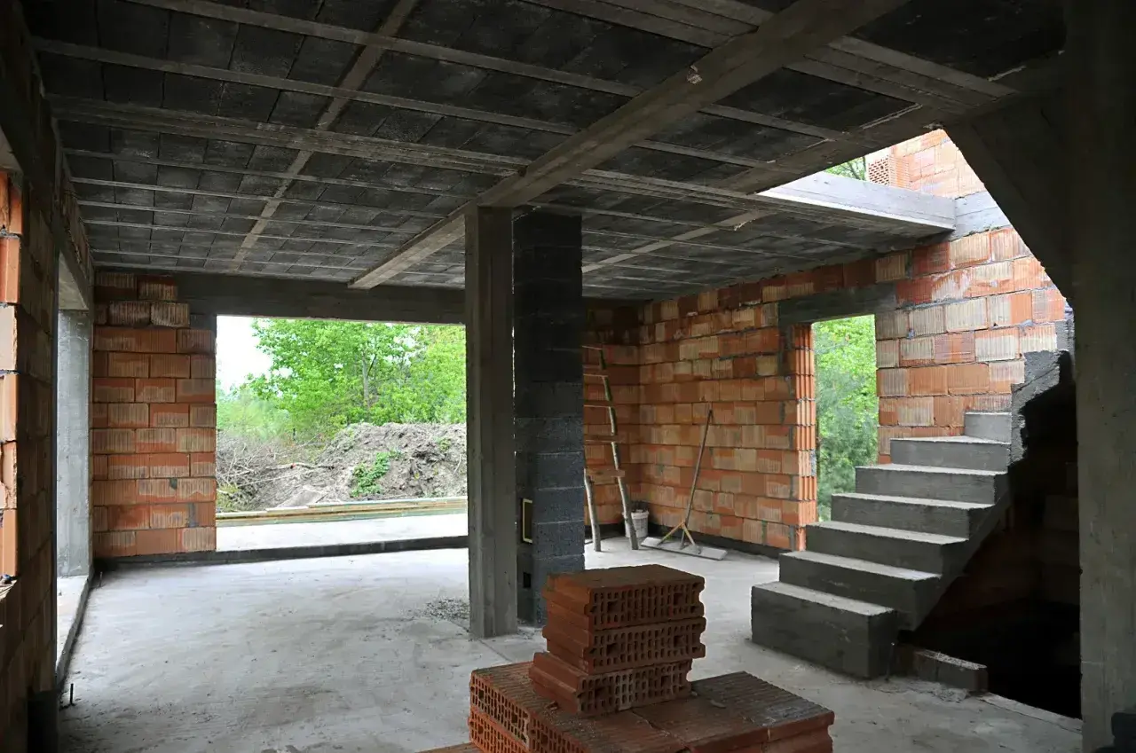 Budowa domu w stanie surowym. Widać strop ackermana, schody, ściany z pustaków i cegieł.