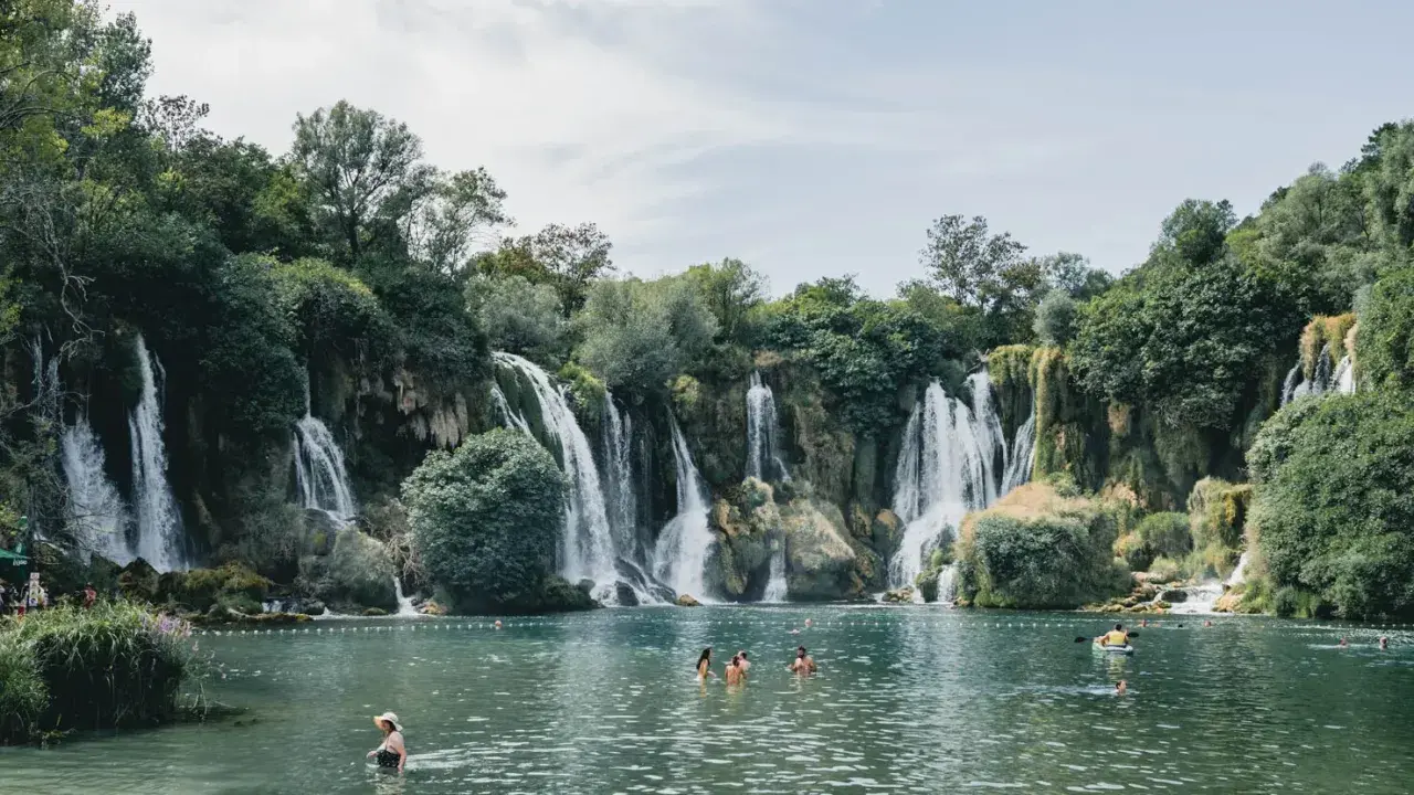Atemberaubende Wasserfälle in Bosnien, Natur pur. Menschen genießen das kühle Wasser in einem türkisfarbenen See, umgeben von üppiger Vegetation.