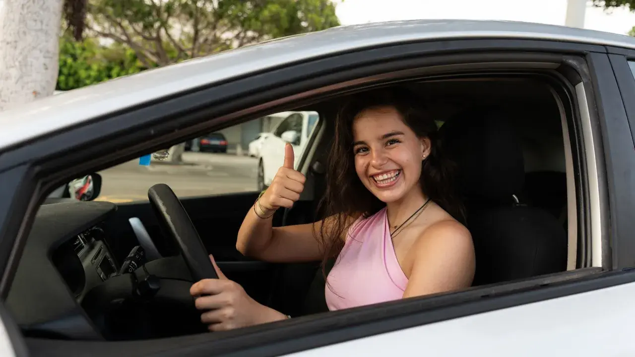 Joven sonriente en coche, pulgar arriba. ¡Ya sabe hasta que edad se puede conducir en España!