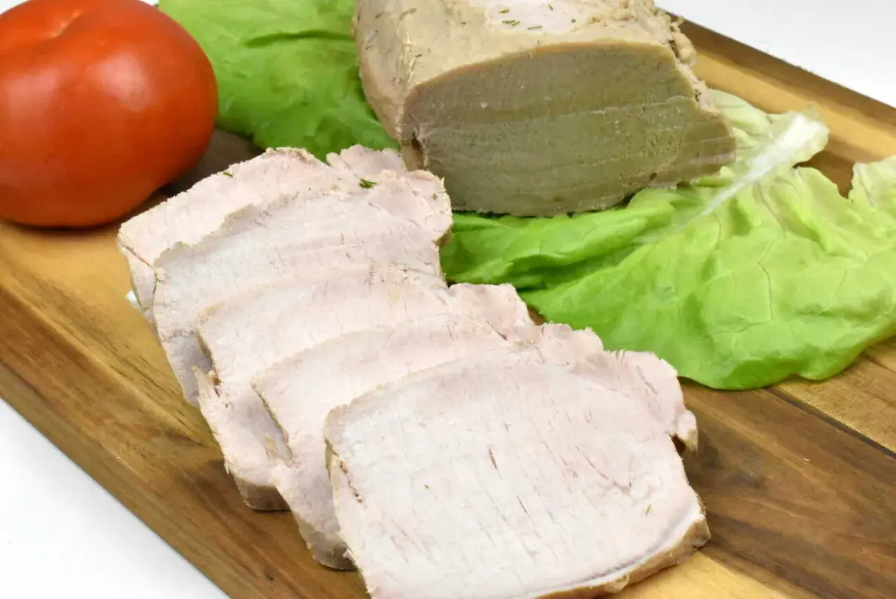 Pokrojony schab gotowany w majonezie, liście sałaty i pomidor na desce.