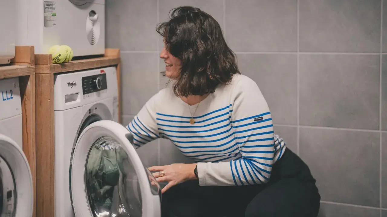 Kobieta w paski wkłada ubrania do pralki. Dowiedz się, jak prać odzież termoaktywną, by służyła latami.