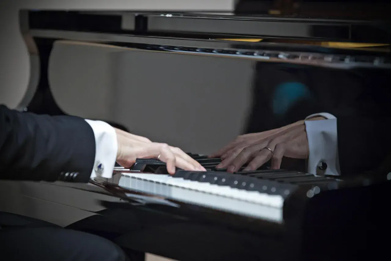 Dłonie muzyka w eleganckiej koszuli i garniturze grają najpiękniejsze utwory na fortepianie, tworząc magiczną melodię.