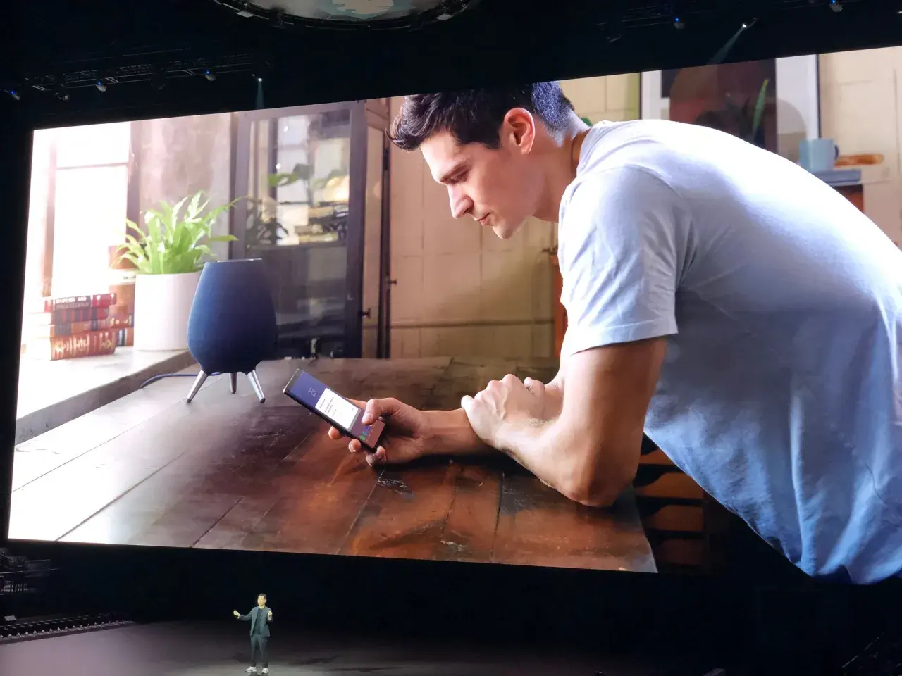Un homme utilise son téléphone pour contrôler son **galaxy home**. Un haut-parleur intelligent est visible sur la table.