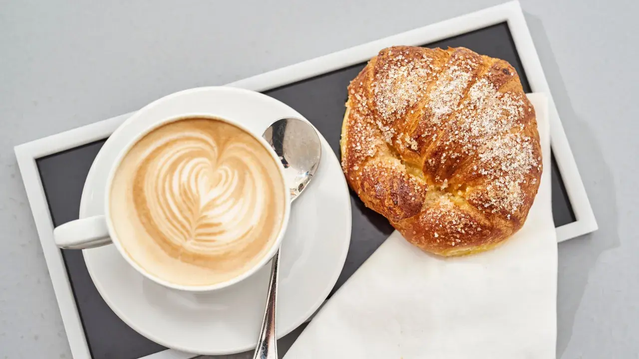 Cappuccino con latte art e brioche americane cosparse di zucchero.